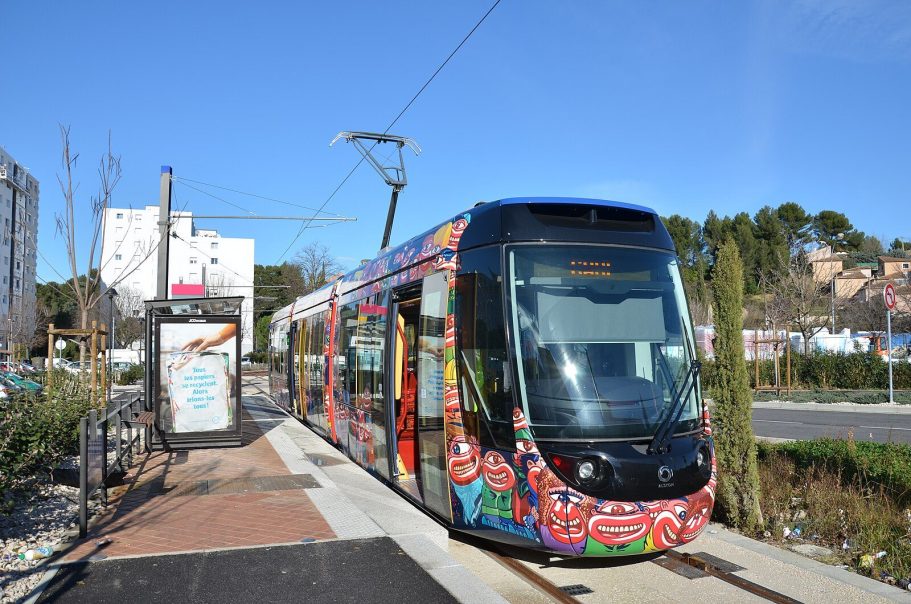 Tram moderno con diseño colorido en una parada de tranvía al aire libre.