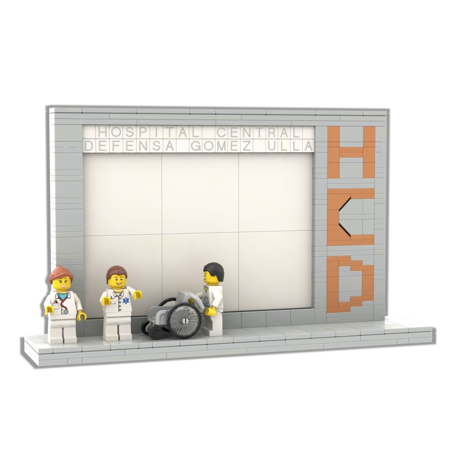Regalos en Miniatura Tres figuras de juguete frente a un panel con un diseño en ladrillos y una silla de ruedas.