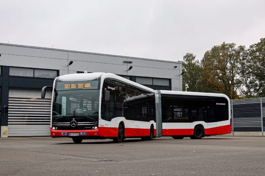 Autobús articulado de colores rojo y blanco estacionado frente a un taller.