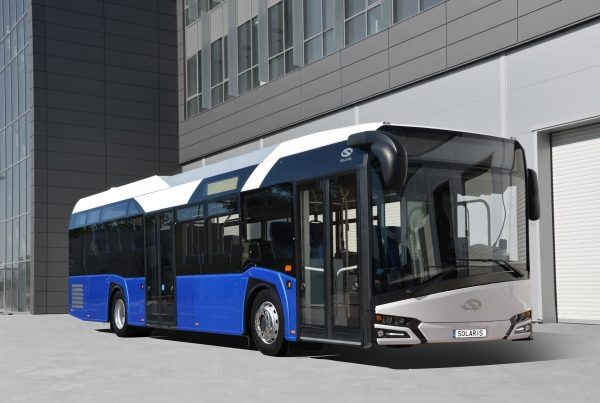 Autobús moderno de color azul y blanco, estacionado frente a un edificio.