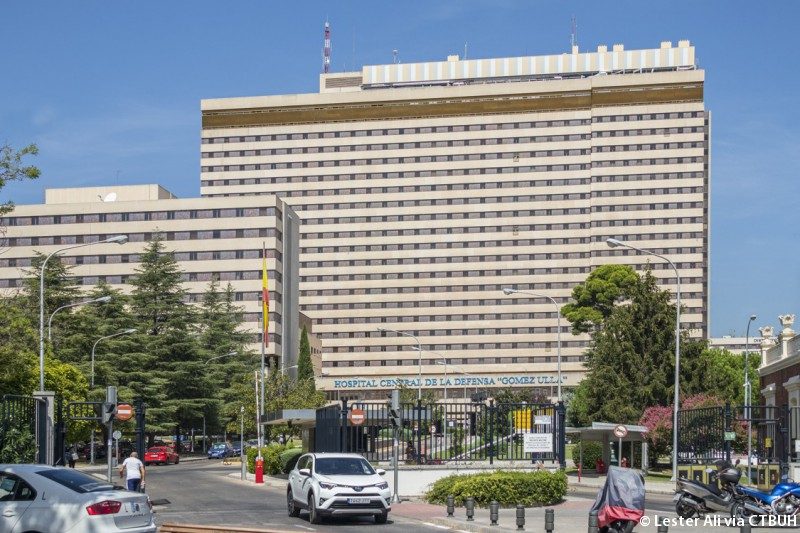 Edificio moderno de varios pisos con vegetación y tráfico en la calle.