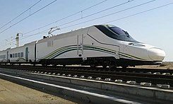 Tren de alta velocidad blanco y verde en vías, con cielo despejado de fondo.