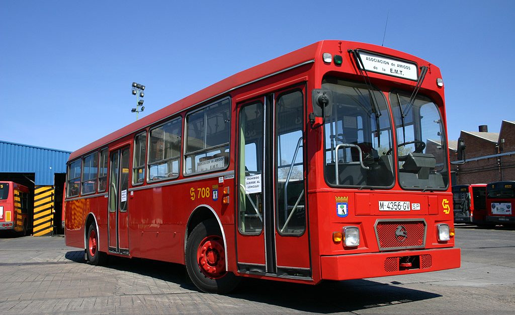 Autobús rojo clásico, aparcado en una estación con cielo despejado.